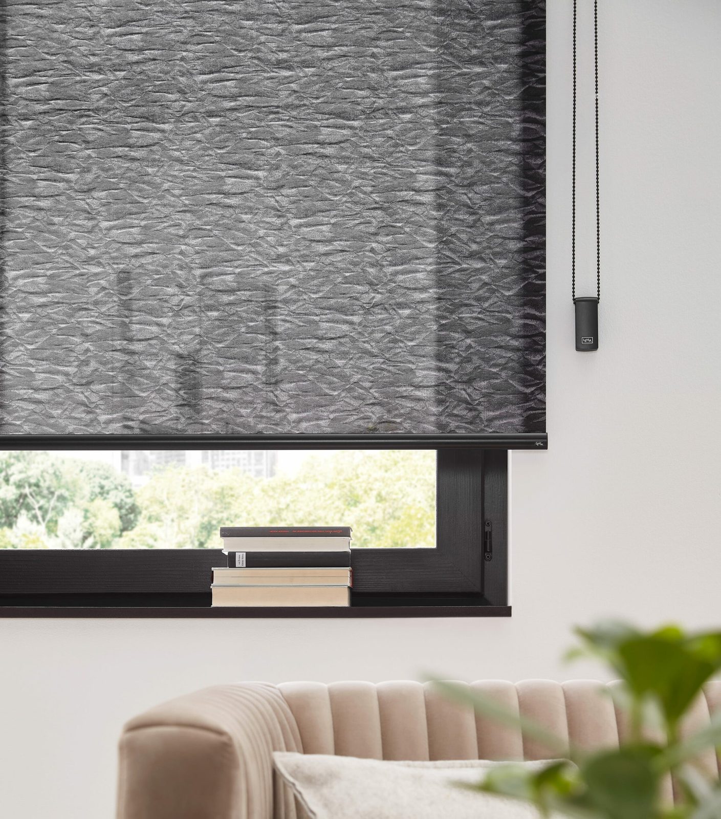 Dunkelgraues Rollo mit Kettenzug vor einem Fenster im Wohnzimmer
